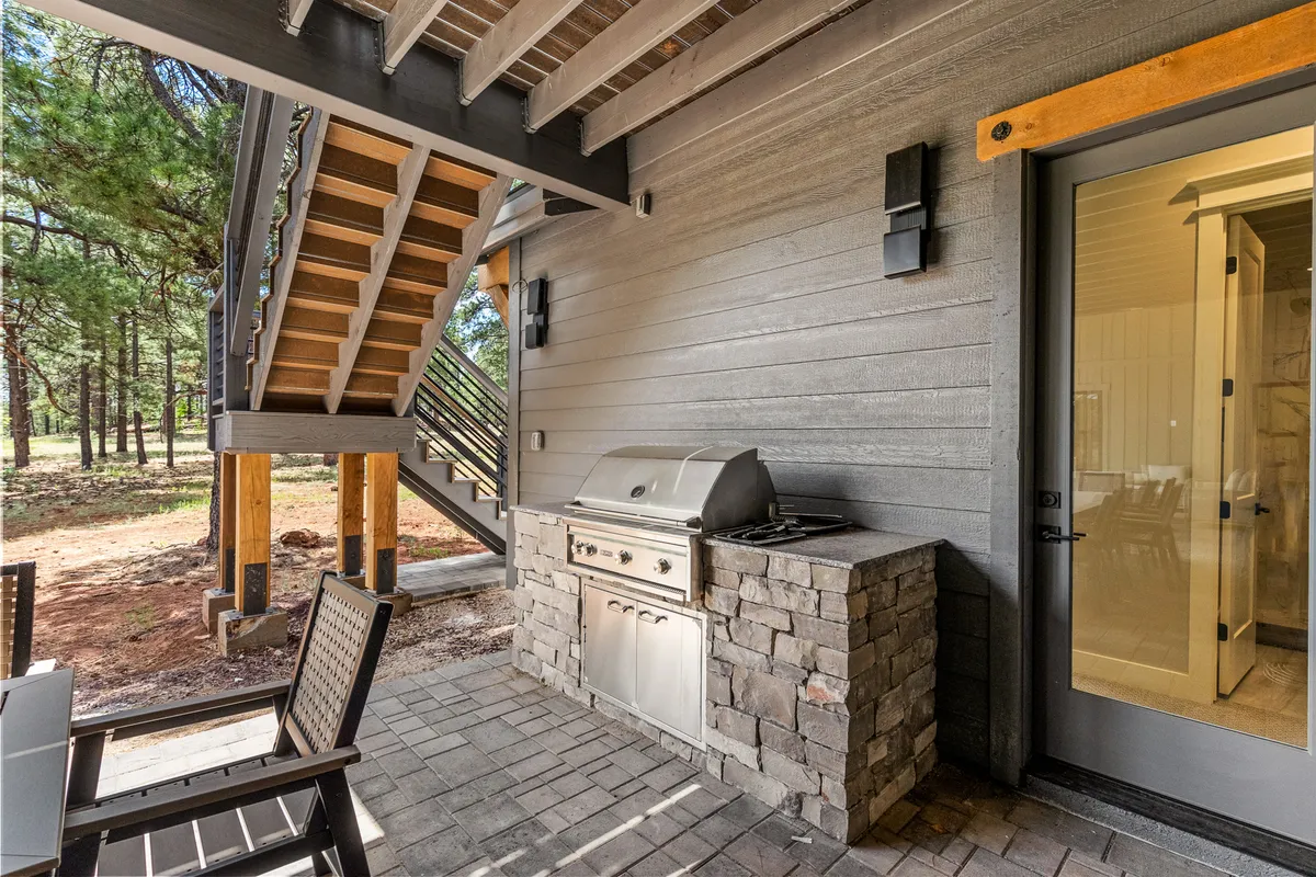 A relaxed and communal outdoor space featuring a grill, abundant seating, and a staircase leading to other parts of the deck or patio. The area is alive with the possibility of barbecues, alfresco meals, and gatherings at sunset.