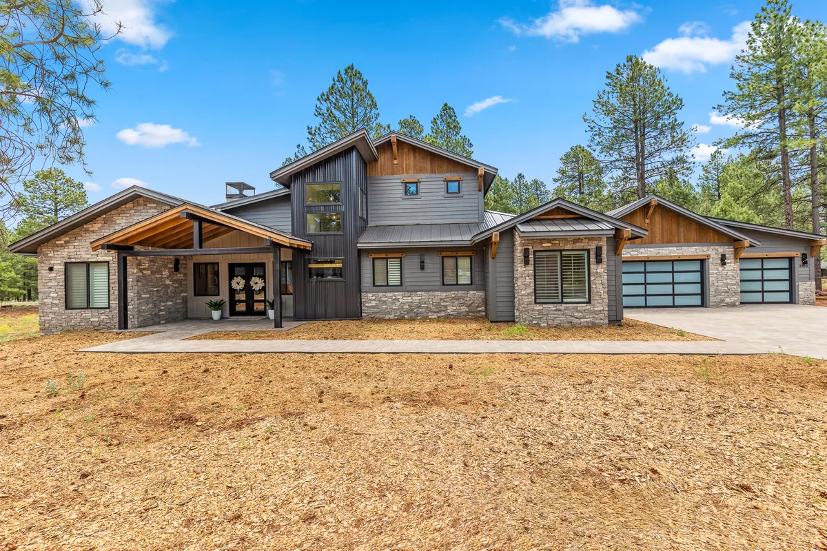 A welcoming view of the home's front entrance, with large windows, a striking stone facade, and visible garage doors. The landscaped approach and driveway suggest convenience and upscale living, while the garage subtly hints at practical amenities like the EV charger mentioned in the content.