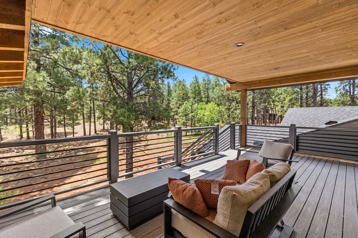 A wooden deck nestled among trees, furnished with comfortable seating. The tranquil setting is ideal for morning coffee, sunset views, and stargazing, surrounded by nature.