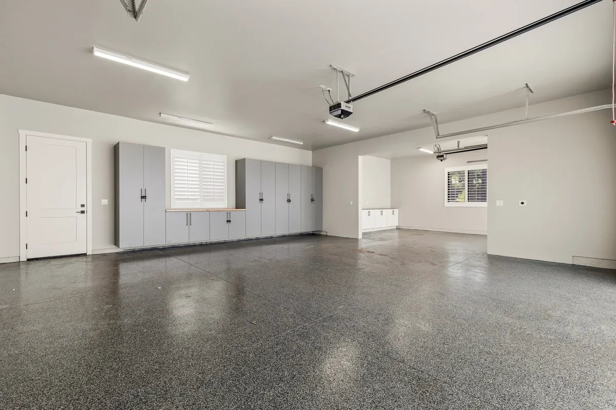 A functional, tidy garage with a spacious floor, storage cabinets, and a window with shutters. The area is well-lit and organized, suitable for parking and storing belongings.