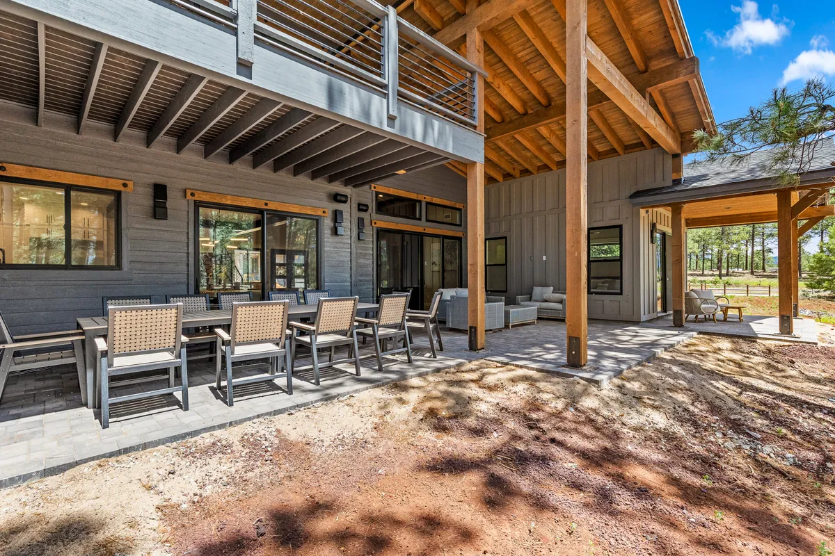 A spacious outdoor dining area with a large table, wooden beams, comfortable seating, and views of the surrounding forest. Glass sliding doors connect the patio to the indoors, creating a seamless flow between spaces.