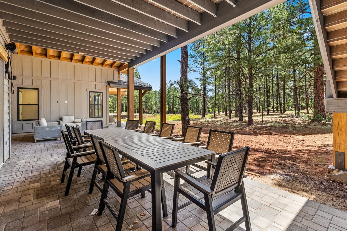 An expansive outdoor dining area nestled among mature trees, featuring a large table and comfortable seating. The setting is ideal for social gatherings, family meals, or simply enjoying a quiet moment outdoors, highlighting the blend of resort-like amenities and natural beauty.