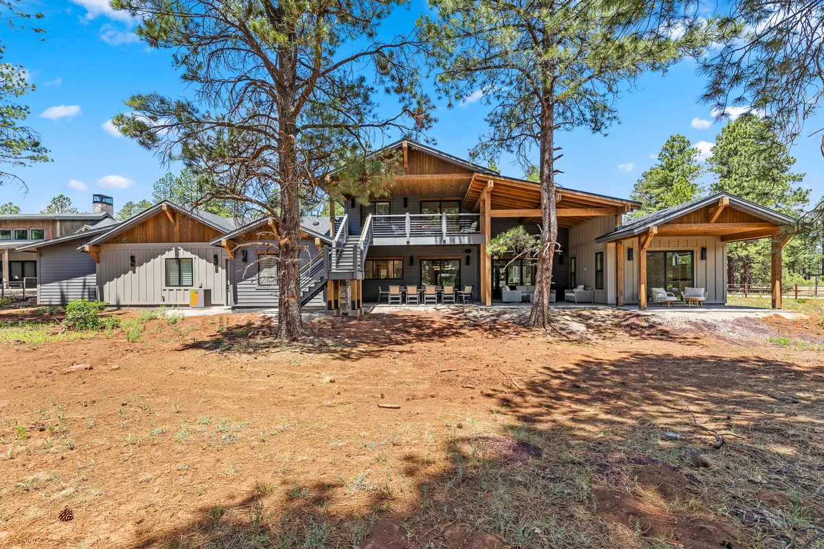 A spacious, modern deck surrounded by tall trees, featuring comfortable seating and a fire pit. The deck is connected to the house, blending indoor and outdoor living, and offers serene views of nature.