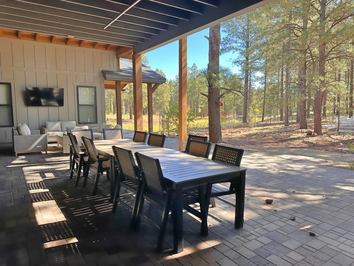 An outdoor dining area nestled among trees with a large table and comfortable seating. The setup is ideal for group meals, celebrations, or relaxed mornings with coffee, surrounded by nature.