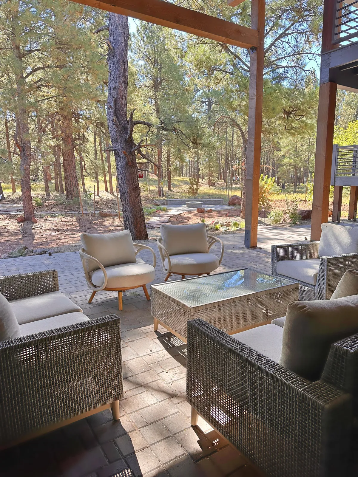 This image showcases a serene outdoor seating area with comfortable chairs and a glass coffee table surrounded by tall pines. The setting exudes calmness, inviting guests to relax, enjoy coffee, and take in the peaceful forest ambiance, perfectly echoing the 'coffee on the deck' experience described in the section.