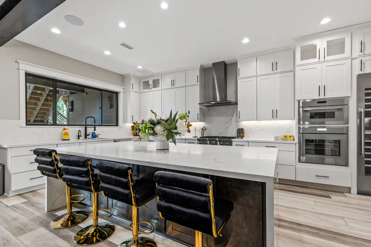 A contemporary kitchen scene with a substantial kitchen island, black velvet bar stools, stainless steel appliances, and fresh flowers in a vase. The design is both stylish and welcoming, featuring spaces ideal for meal prep, casual breakfasts, and socializing.